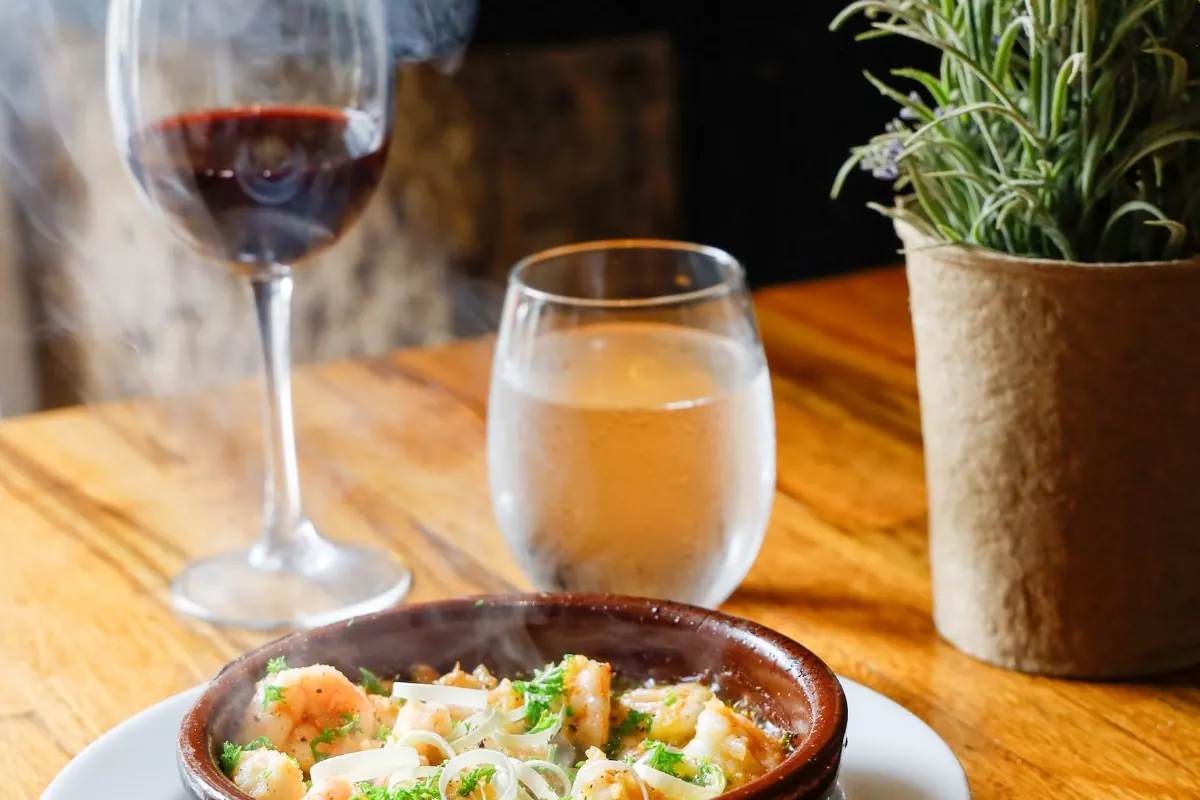 Cazuela humeante y copa de vino tinto sobre mesa de madera